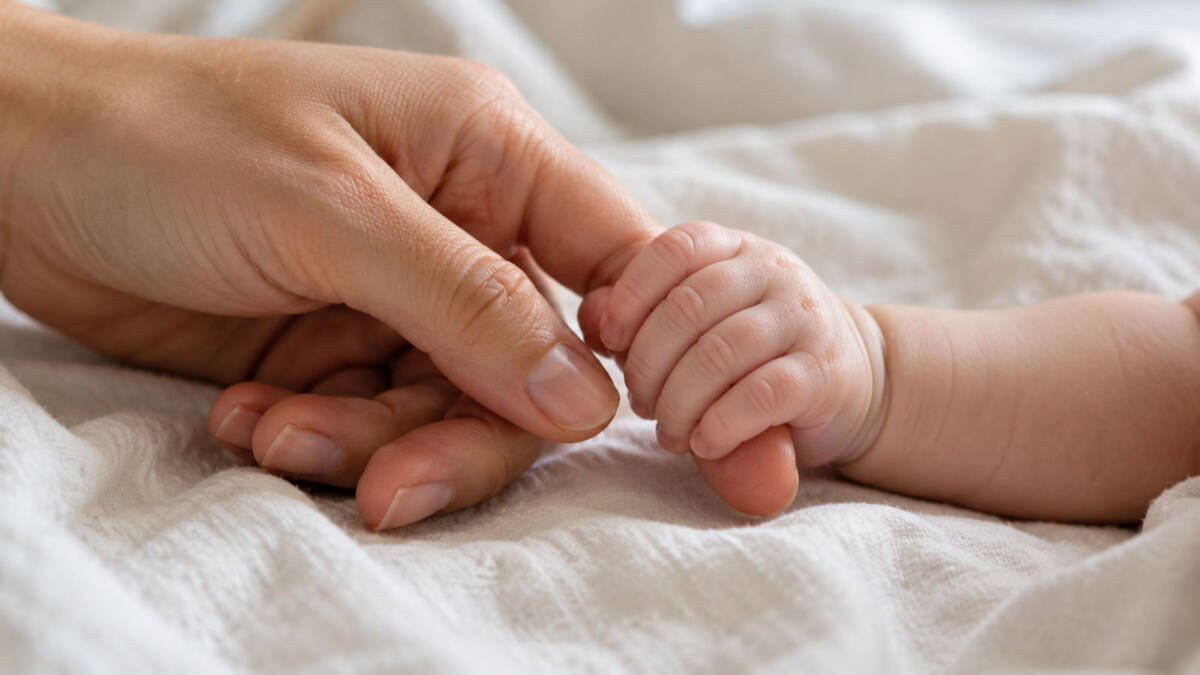 natalita-toscana-contributo-neomamme-2027 Una mano adulta stringe delicatamente la mano di un neonato.